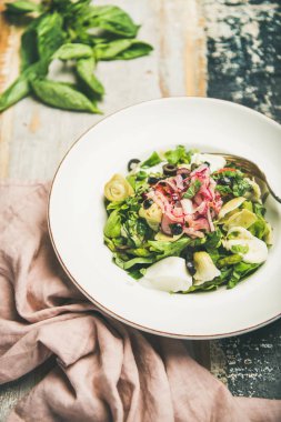 Arka plan boya taze yeşil yaz salatası enginar, zeytin, peynir ve rustik ahşap üzerinde beyaz tabak içinde kırmızı soğan ile