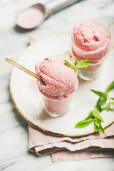Healthy low calorie summer dessert. Homemade strawberry yogurt ice cream with fresh mint in glasses on plate over grey marble table background.