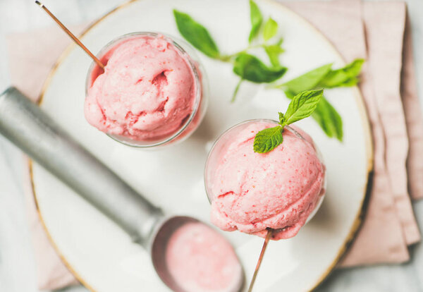 Healthy low calorie summer dessert. Homemade strawberry yogurt ice cream with fresh mint in glasses on plate over light grey marble table background