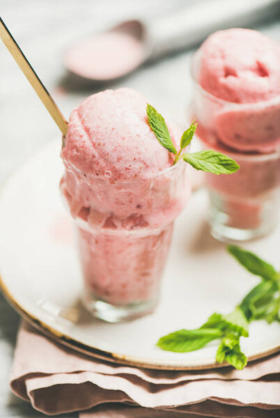 Homemade strawberry yogurt ice cream with fresh mint in glasses on plate over grey marble background