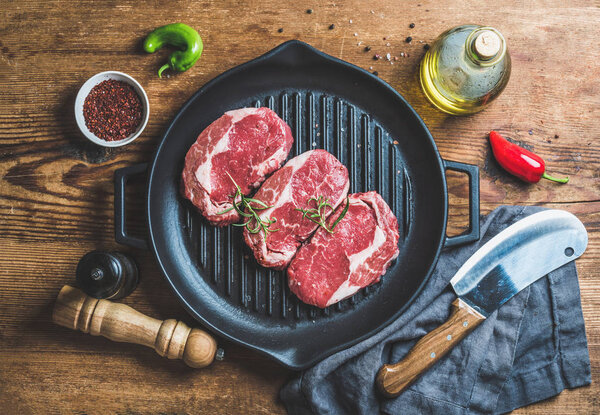 Ingredients for cooking Rib eye roast beef steak on black iron grilling pan over wooden background