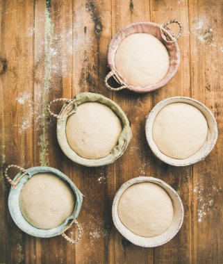 Sourdough for baking homemade wheat flour bread in baskets, over rustic wooden kitchen table background clipart