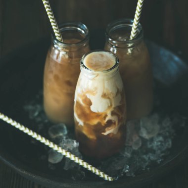 Soğuk Tay buzlu çay plaka üzerinde süt ile cam şişelerde karanlık ahşap arka plan üzerinde