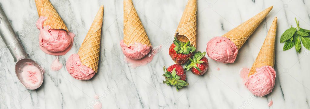 Homemade yogurt ice cream with strawberries in waffle cones over grey marble background