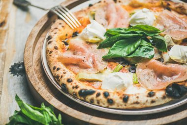 Taze pişmiş pizza enginarlı, Füme hindi jambon, zeytin, krem peynir ve fesleğen rustik ahşap arka plan üzerinde