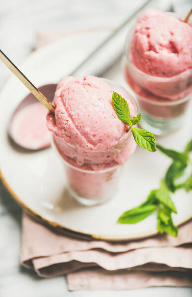 Homemade strawberry yogurt ice cream with mint in glasses over light grey marble table background