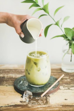 Buzlu matcha latte ile Hindistan cevizi sütü kadının el, beyaz arka plan, duvar ve bitki şubeleri sürahi dökme cam içki