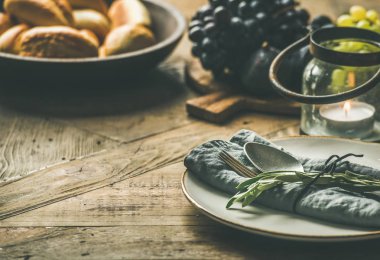 Sonbahar tatil sofra dekorasyon. Plaka gri kumaş peçete, çatal ve kaşık, mum, Yönetim Kurulu, ekmek buns, zeytin ağacı dalı ahşap arka plan üzerinde hizmet üzerinde üzüm ile