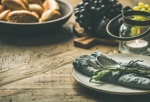 Sonbahar tatil sofra dekorasyon. Plaka gri kumaş peçete, çatal ve kaşık, mum, Yönetim Kurulu, ekmek buns, zeytin ağacı dalı ahşap arka plan üzerinde hizmet üzerinde üzüm ile