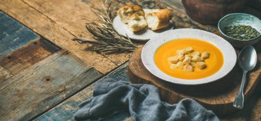 Kabak kremalı çorba, kruton ve tohum gemide rustik ahşap arka plan üzerinde ısınma düşmek