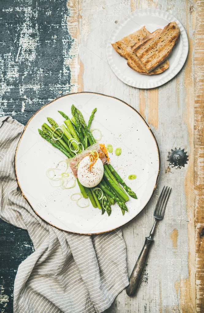 green asparagus with soft-boiled egg, leek and bacon served in white plate and grilled bread over linen napkin and rustic wooden background