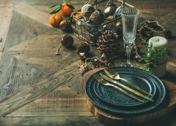 Christmas or New Year eve holiday table setting. Plates, silverware, glass, pine cone, candle and toy festive decorations over vintage table background