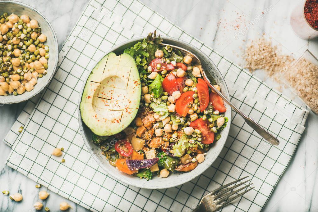 Vegan lunch bowl. Dinner with avocado, mixed grains, beans, sprouts, greens and vegetables over marble table background