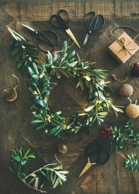 Noel için hazırlanıyor. Yeşil zeytin dalı Festival çelenk, Noel ağacı dekorasyon oyuncak, hediye kutusu ve makas rustik ahşap masa arka plan üzerinde