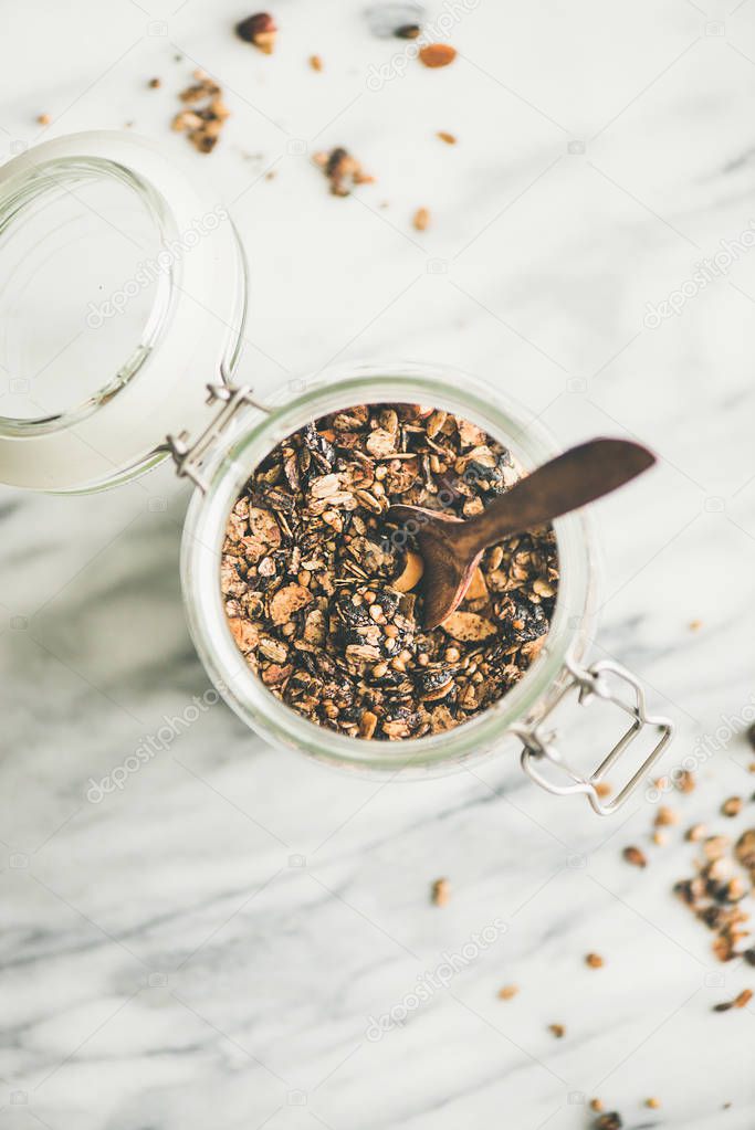 Healthy breakfast preparation. Buckwheat and chocolate granola with hazelnuts in jar with spoon over light marble background
