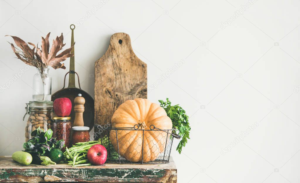 Autumn seasonal food ingredients, kitchen utensils. Vegetables, pumpkin, apples, canned food, fallen leaves over rustic wooden chest of cupboard