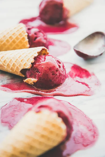 Melting natural raspberry sorbet ice-cream scoops in sweet waffle cones over light marble background
