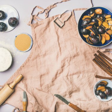 Fırın malzemeleri ve araçları. Tozlu pembe keten önlük, mutfak gereçleri, un, şeker, meyve ve baharat pastel leylak arka plan üzerinde