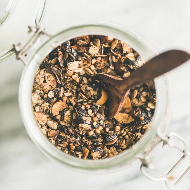 Sağlıklı kahvaltı hazırlığı. Açık renkli mermer üzerine kaşıkla kavanoza fındık ile buğday ve çikolata granola