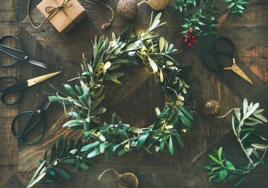 Noel için hazırlanıyor. Yeşil zeytin dalı Festival çelenk, Noel ağacı dekorasyon oyuncak, hediye kutusu ve makas rustik ahşap masa arka plan üzerinde