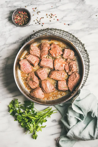 Meat dinner. Braised beef meat stew with fresh parsley in cooking pan over white marble table background. — Stock Image Meat Dinner Braised Beef Meat Stew Fresh Parsley Cooking Pan Royalty Free Stock Photos
