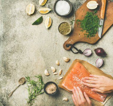 Pişirme Somon Balık tuzlu. Çiğ somon fileto, kadın el koyarak tuz ve otlar gri beton arka plan üzerinde füme