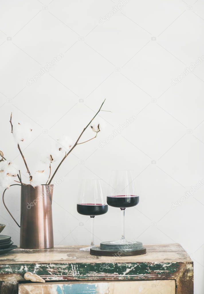 Two glasses of red wine over rustic kitchen countertop, white background behind