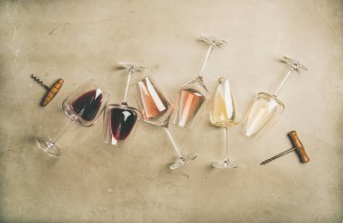 Red, rose and white wine in glasses and corkscrews over grey concrete background clipart