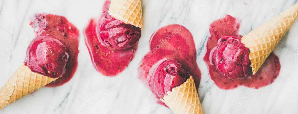 Fresh summer dessert. Red melting natural raspberry sorbet ice-cream scoops in sweet waffle cones over light marble background