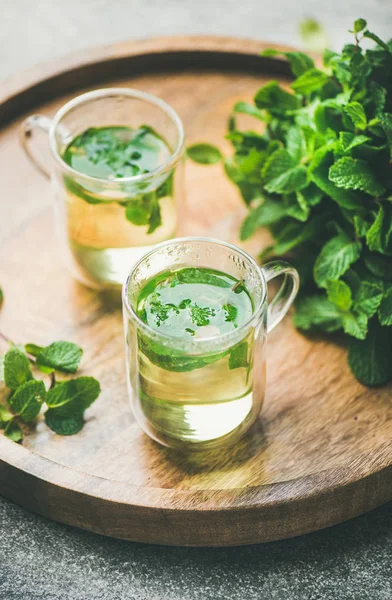 stock image Hot herbal mint tea drink in glass mugs over wooden tray with fresh garden mint leaves