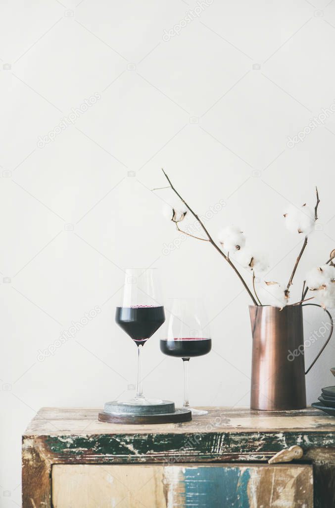 Two glasses of red wine and flowers over rustic kitchen countertop, white background behind