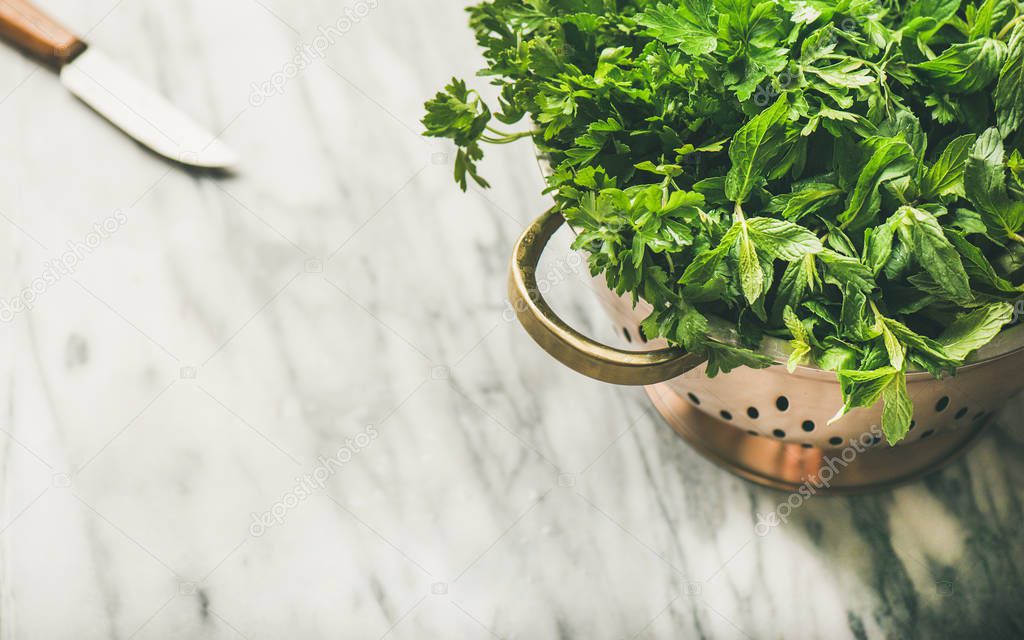 Bunch of fresh green garden herbs in brass colander over marble kitchen table background