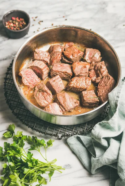 stock image Meat dinner. Braised beef meat stew with fresh parsley in cooking pan over white marble table background