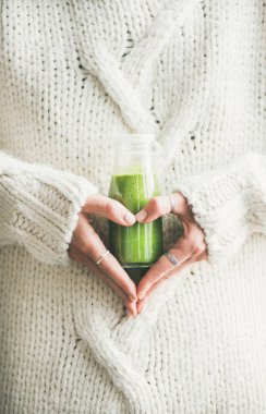 Kış mevsimlik güler yüzlü detoks iç. Sıcak kazak yeşil smoothie veya elleri kalp şekil verme suyu şişe tutan kadın. Yeme, kilo verme, sağlıklı diyet gıda kavramı temiz