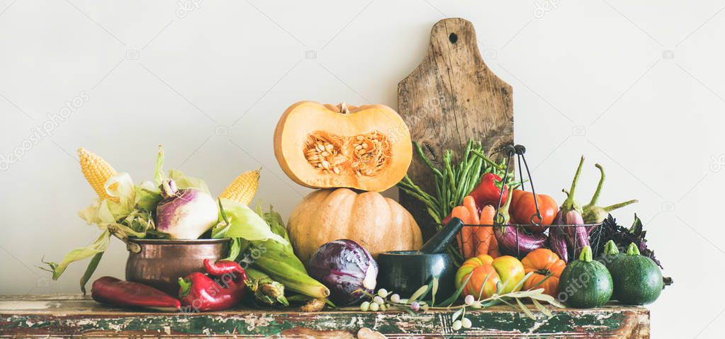 Fall vegetarian food ingredients variety. Assortment of Autumn vegetables for healthy cooking over rustic cupboard, white wall background, copy space, wide composition. Local market organic produce