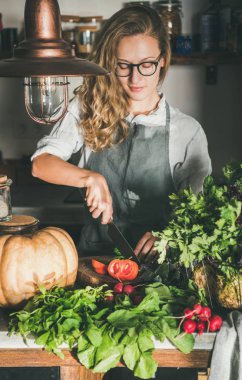 Mevsimlik vejetaryen veya vegan yemek düşer. Genç kadın keten önlük kesme taze otlar ve beton mutfak tezgahı sebze. Yavaş gıda, comfort gıda, sağlıklı beslenme, beslenme temiz