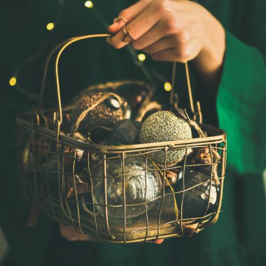 Tel sepet dolu yeşil şenlikli elbise, tatil çelenk ışıklar bokeh arka plan, seçici odak, kare kırpma, kadının elinde Noel ve yeni yıl ağacı altın vintage dekorasyon oyuncak
