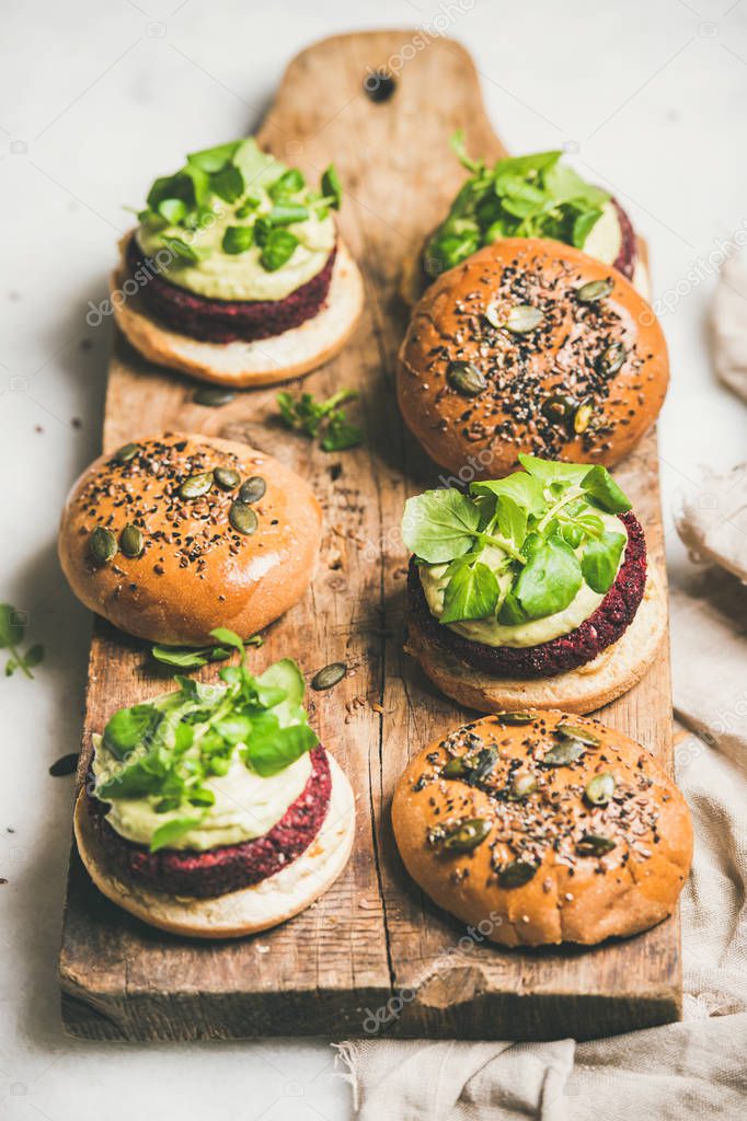 Healthy vegan burgers with quinoa beetroot patties, avocado cream and green sprouts on wooden board over light background, selective focus . Vegetarian, clean eating food