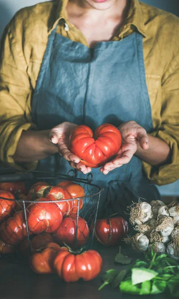 トマトソース 缶詰のトマトやバジルとニンニク キッチン カウンターでパスタを調理するため先祖伝来の熟したトマトを保持しているリネンのエプロンの女性 — ストック写真