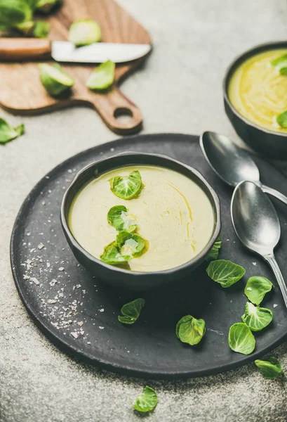 Seasonal brussels sprouts vegetable cream soup in dark bowl and fresh green brussel sprouts over grey concrete background, vertical composition. Vegan, vegetarian, healthy, dieting food concept — Stock Image Seasonal Brussels Sprouts Vegetable Cream Soup Dark Bowl Fresh Green Stock Photo