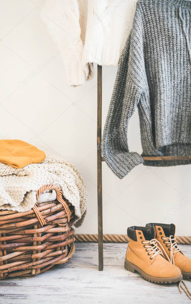 Fall or winter warm knitwear on hanger, white wall background. Fashionable female winter clothing. Woolen sweaters, boots and knitted hat