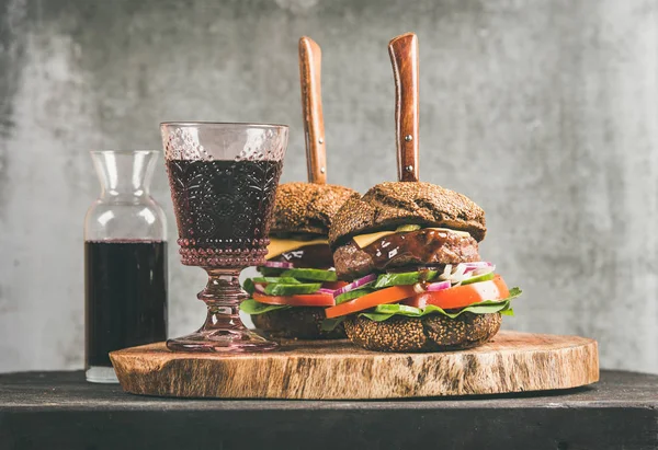 バーベキュー ソースと牛肉肉ハンバーガーや素朴な木の板 背景に灰色のコンクリートの壁に赤ワインのガラス 快適な食べ物 ハンバーガー ビストロ コンセプト — ストック写真