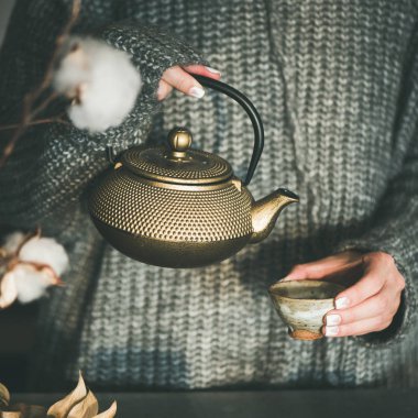 Çay töreni. Genç kadın gri sıcak örme kış kazak dökme yeşil çay mutfak, Japon seramik Kupası Altın demir pota dan kare kırpma. Soğuk kış sabahı evde