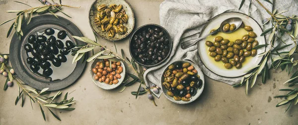 平放置各种地中海腌制橄榄在盘子和碗和橄榄树树枝在灰色的混凝土桌的背景 顶视图 地中海梅泽开胃菜 — 图库照片