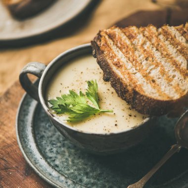 Sonbahar, kış eve akşam yemeği. Kereviz krem çorba Kupası ve tost ısınma sarı keten masa örtüsü, yakın çekim, kare kırpma düşmek. Konfor gıda, vegan, Vejetaryen, sağlıklı ve yavaş gıda kavramı