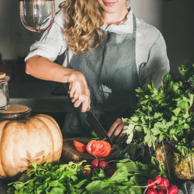 Mevsimlik vejetaryen veya vegan yemek düşer. Genç kadın önlük kesme taze otlar ve beton mutfak tezgahı, sebze kare kırpma. Yavaş gıda, comfort gıda, sağlıklı beslenme, beslenme temiz