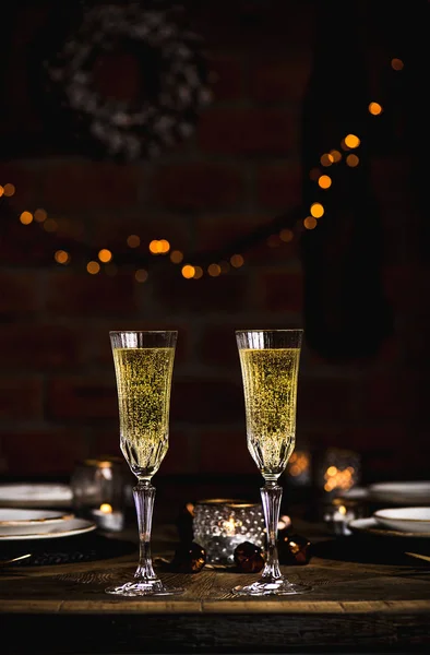 クリスマス シャンパン キャンドル装飾おもちゃ 花輪の背後にあるれんが造りの壁に輝くガーランドのメガネで新年祝いセット 木製のテーブル 休日のお祝い 新年の夜 — ストック写真