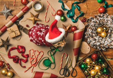 Noel ve yeni yıl tatil için hazırlanıyor. Düz-lay süslemeleri, şeritler, hediye kağıt, kapı çelengi, topları, şekerler ve kedi kırmızı kış Noel kazağı ve Kürk kap, parlak görünümü top