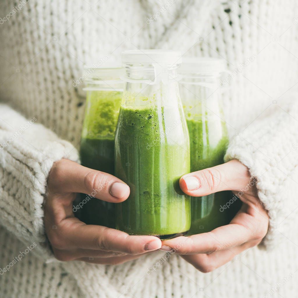 Winter seasonal smoothie drink detox. Female in light knitted sweater holding bottles of green smoothie or juice in her hands, square rop. Clean eating, weight loss, healthy dieting food concept