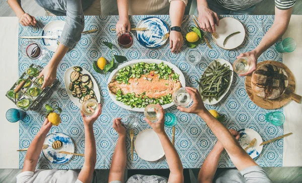 地中海风格的晚餐 平铺的桌子配熟的三文鱼 开胃菜 面包在蓝色桌布上 手拿着饮料 分享食物 顶视图 假日派对理念 — 图库照片